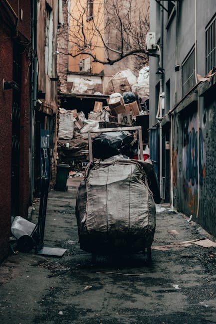 A large pile of black plastic rubbish bags, some with visible tears and loose edges, stacked against a modern exterior wall composed of beige tiles with visible grout lines. The bags contain assumed w